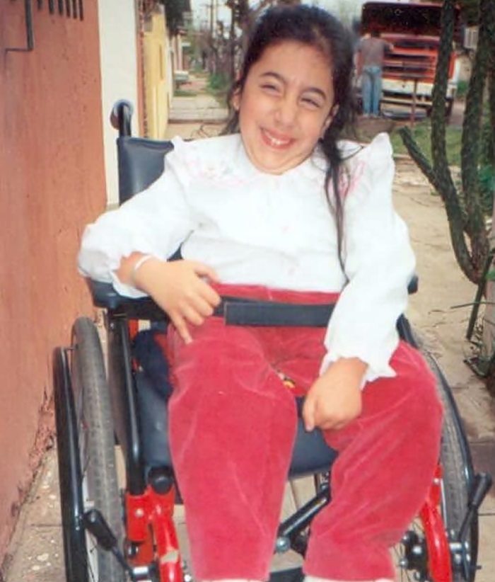 Sentada en su silla de ruedas, como de 7 años, Daiana sonríe a cámara. 