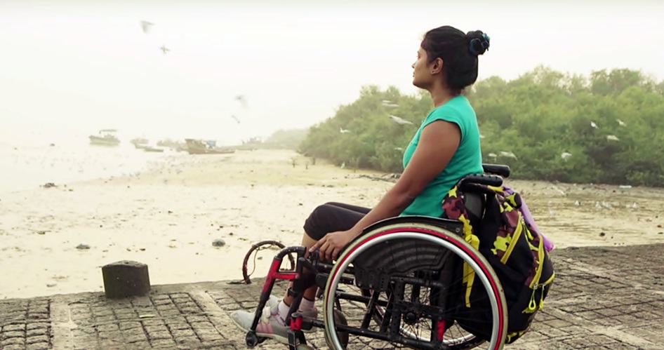 En un muelle, sentada en su silla de ruedas, Nisha  observa el horizonte de una playa en donde vuelan gaviotas.
