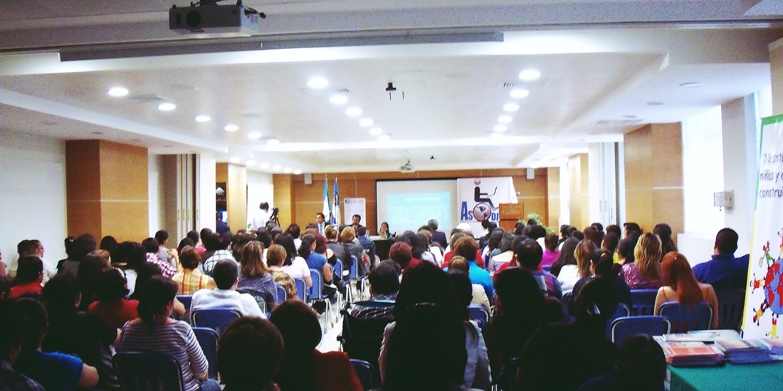Un auditorio universitario de Guatemala se ve repleto de público, al fondo una mesa con los conferencistas y una manta con el logo de Asodispro