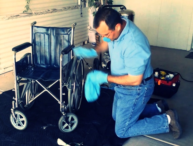 Un hombre de rodillas limpia una silla de ruedas