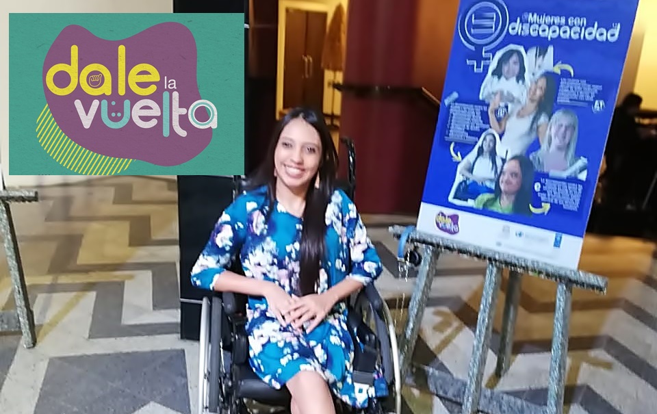 María José posa en su silla de ruedas junto a un afiche de la campaña "Dale la Vuelta"