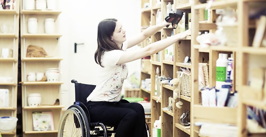 Una mujer en silla de ruedas ordena unos estantes. Fotografía a manera de ilustración del tema. 