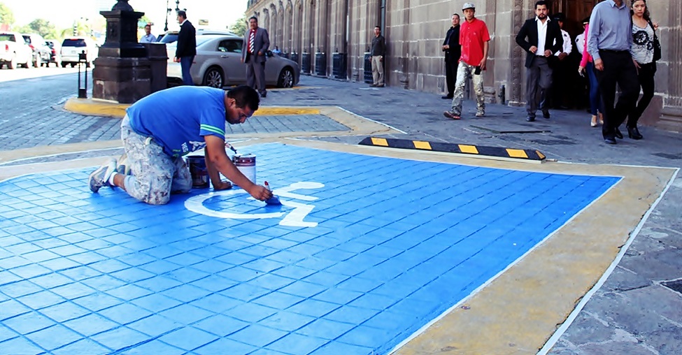 Un hombre pinta con una brocha el símbolo internacional de accesibilidad en el estacionamiento de un edificio 