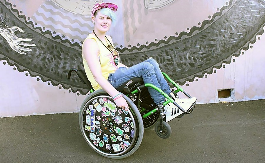 La atleta rubia, en su silla de ruedas en dos llantas, sonríe a cámara, en camiseta y jeans. 