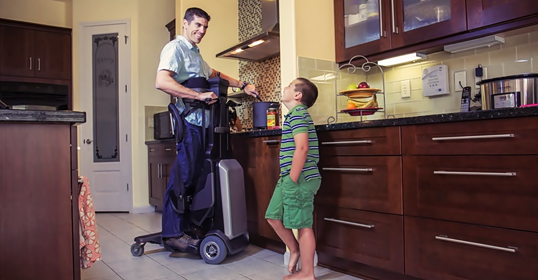 Un niño observa a un hombre de pie mediante el dispositivo de su silla de ruedas