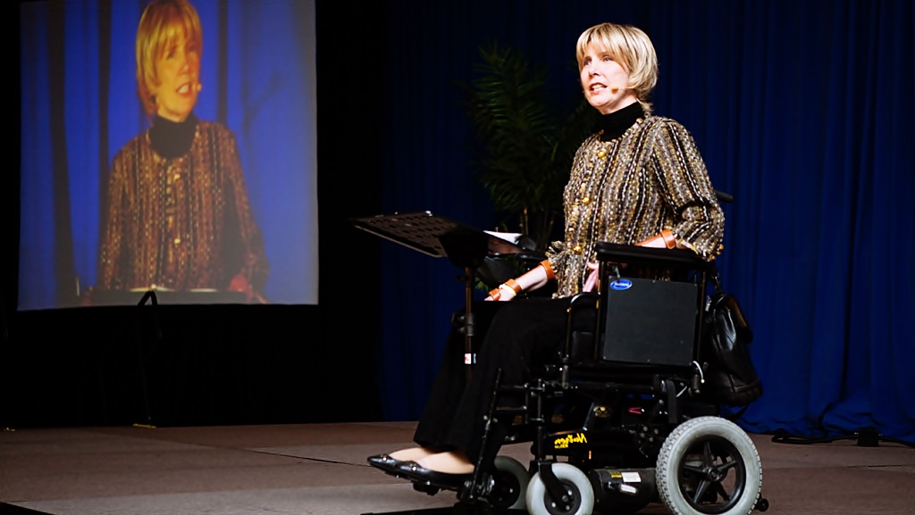 En su silla de ruedas eléctrica Joni Tada realiza una conferencia en un escenario 