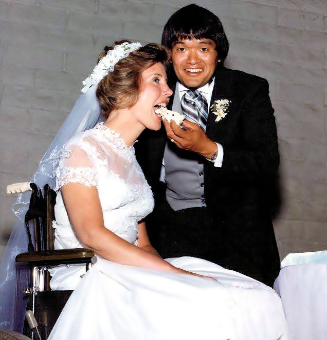 Ken da en la boca un pedazo de pastel de bodas a Joni, quien está en su silla de ruedas y vestida de novia.