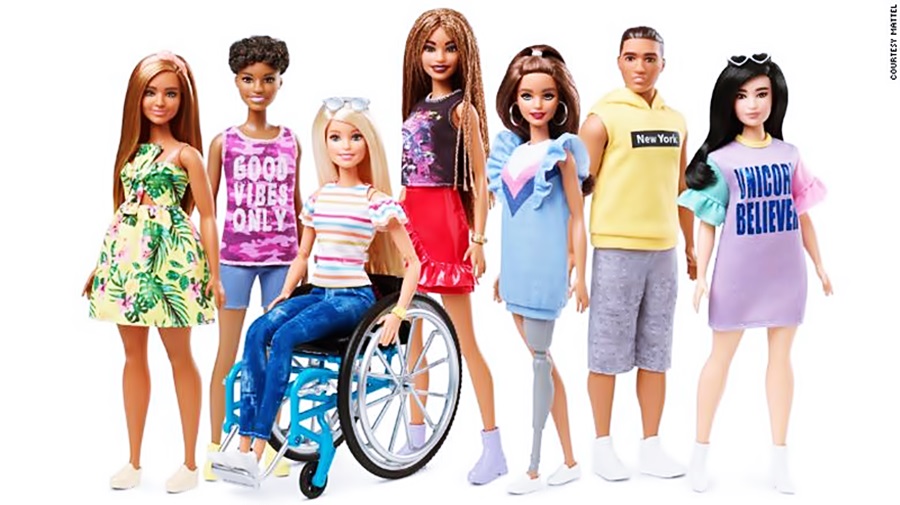 entre varias muñecas, se ve una en silla de ruedas y otra con una pierna con prótesis 