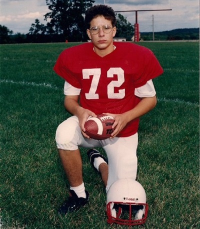 Scott luce su uniforme de futbol americano, hincado en uno de sus pies y con un balón entre sus manos, tendría cómo 14 años. 