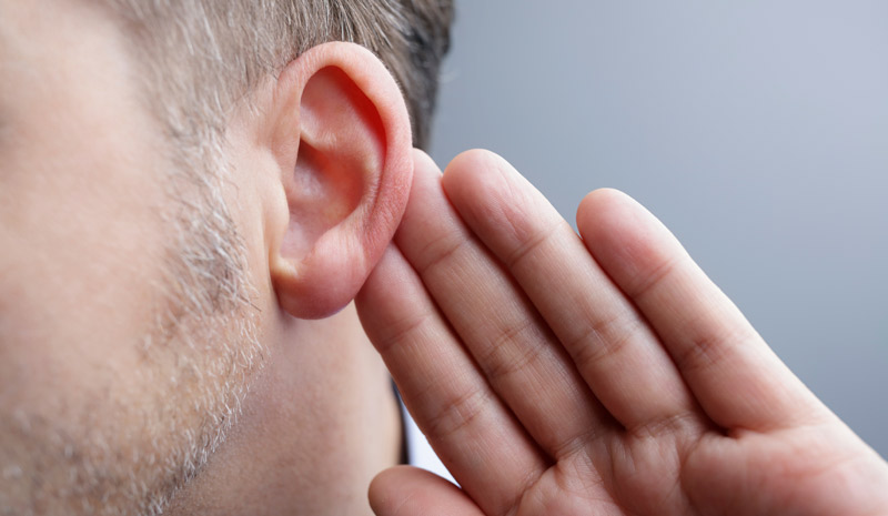 Fotografía de la oreja de una persona, con la mano a su lado en señal de intentar escuchar más