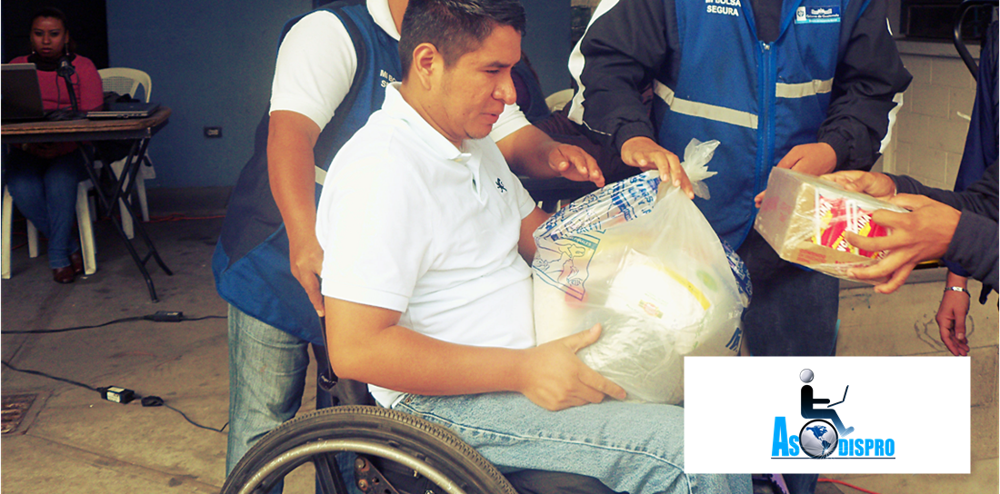 Un beneficiado de Asodispro en silla de ruedas recibe bolsa  de alimentos