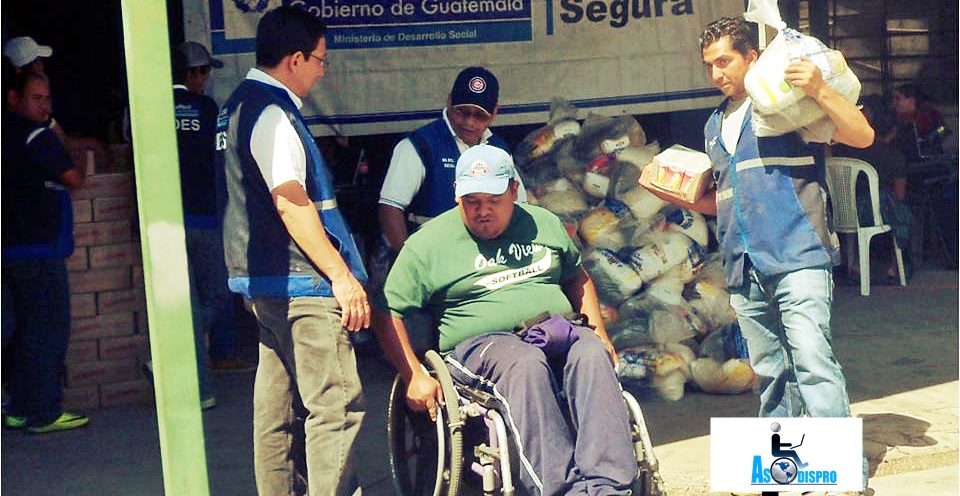 Una persona en silla de ruedas es ayudado por personeros del ministerio para llevar su bolsa de alimentos