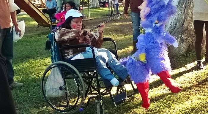 Gaby rompe una piñata desde su silla de ruedas durante un Paseo Navideño Asodispro
