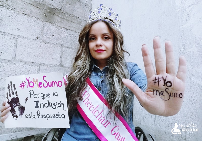 Sentada en su silla de ruedas con su corona y banda de Miss Wheelchair Guatemala, María sostiene un cartel que dice: Yo me sumo, porque la inclusión es la respuesta. Tiene la palma de la una de sus manos frente a la cámara y se lee el hashtag: Yo me sumo.