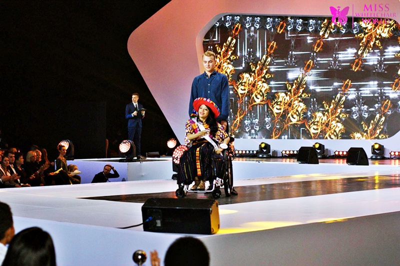 El momento en que la representante de Guatemala luce su traje regional, la silla de ruedes es empujada por un caballero.