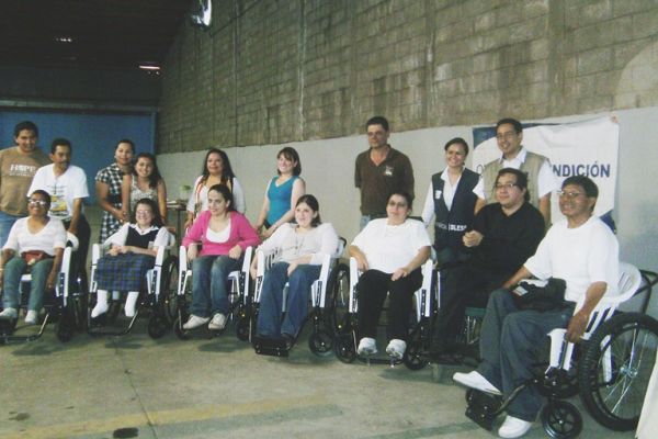 Byron Pernilla está junto a otras 7 personas en silla de ruedas, atrás de ellos varias personas sin discapacidad. Esto luego de entregar la donación de sillas de ruedas.