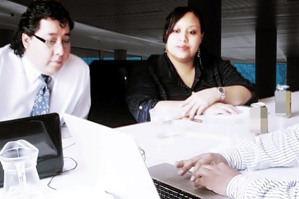 En una mesa de trabajo, un ejecutivo muestra a Byron Pernilla y Lissete Véliz la pantalla de una computadora  durante una capacitación.