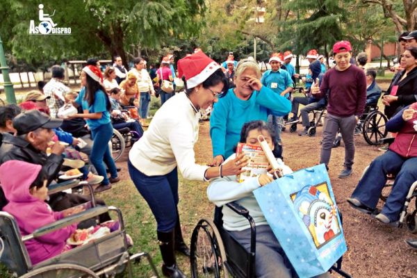 La directora de Contacto Humano, entrega un presente navideño a una persona en silla de ruedas.