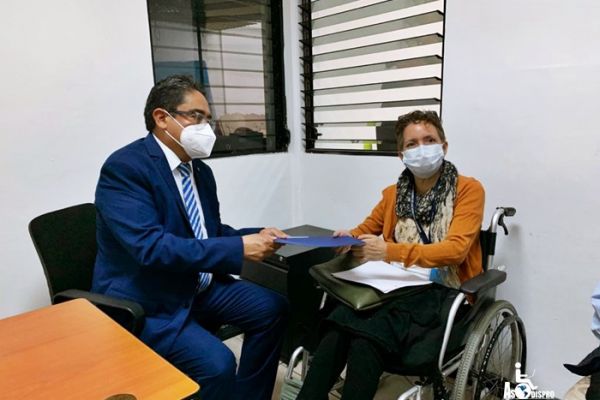 Durante la visita al PDH Maribel Palencia en su silla de ruedas y el Lic. Rodas sentado, se toman una fotografía entregando documentos.