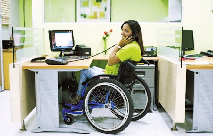 Una chica en silla de ruedas contesta un teléfono en un cubículo de una empresa.