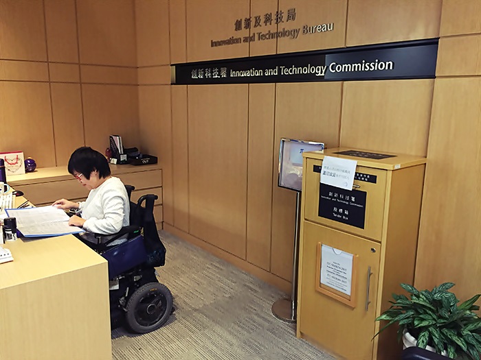 Una joven en silla de ruedas eléctrica, revisa papelería en la recepción de una empresa