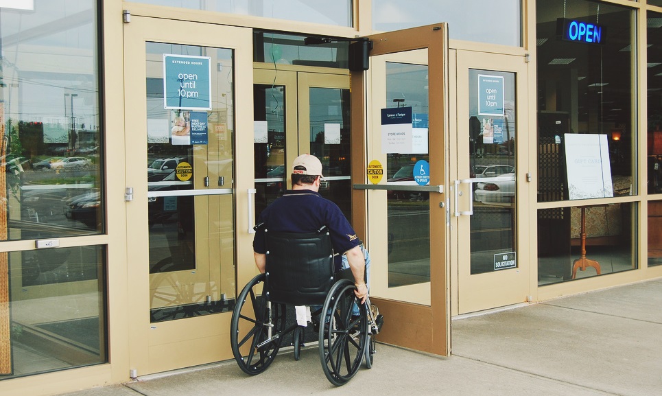 Un hombre en silla de ruedas intenta entras a un edificio con puertas de cristal