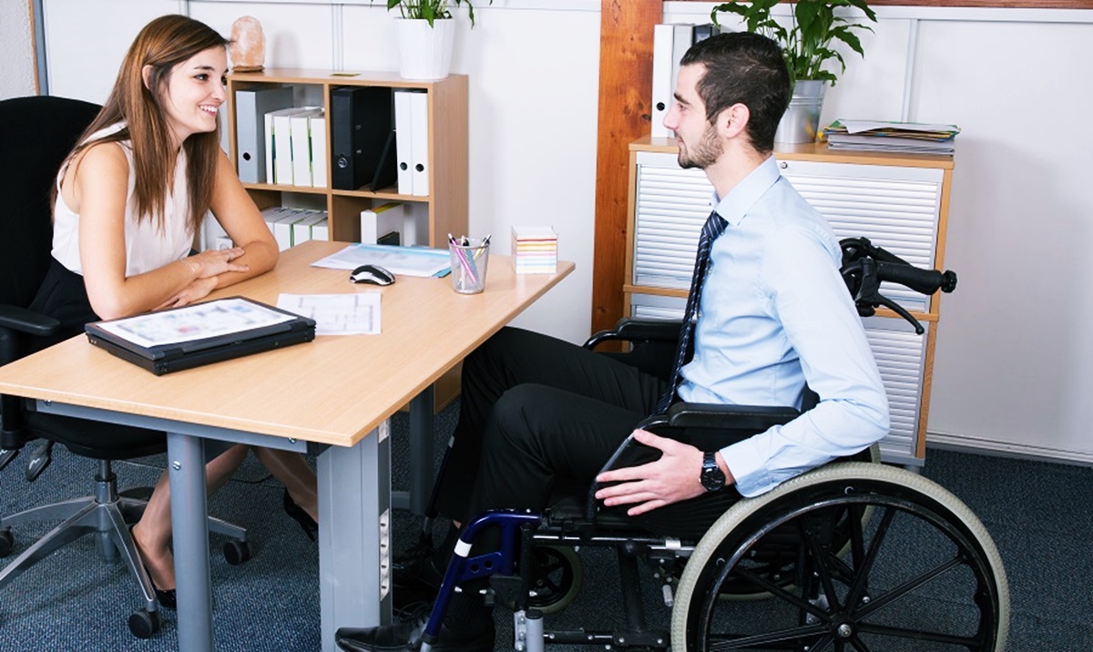 Una joven entrevista en el escritorio de una oficina a un joven de corbata en silla de ruedas 